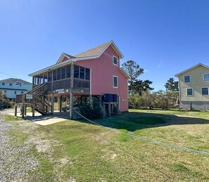 A two-story house with a balcony, a covered porch, and a grassy yard. - Potter's Place: Pet-friendly Peaceful Location (Ocracoke)
