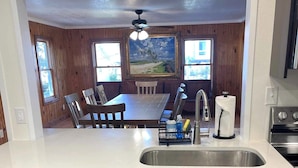 A kitchen with a central island, a dishwasher, dark cabinets, a sink, and a ceiling fan. - Stay Salty: Recently Renovated Historic Home l Centrally Located I Pet Friendly (Ocracoke)