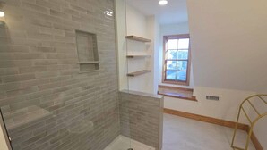 A bathroom with a glass shower enclosure, a window, and a wooden shelf unit. - Stay Salty: Recently Renovated Historic Home l Centrally Located I Pet Friendly (Ocracoke)