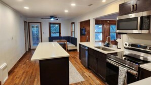 A modern kitchen with a central island, stainless steel appliances, and wooden flooring. - Stay Salty: Recently Renovated Historic Home l Centrally Located I Pet Friendly (Ocracoke)
