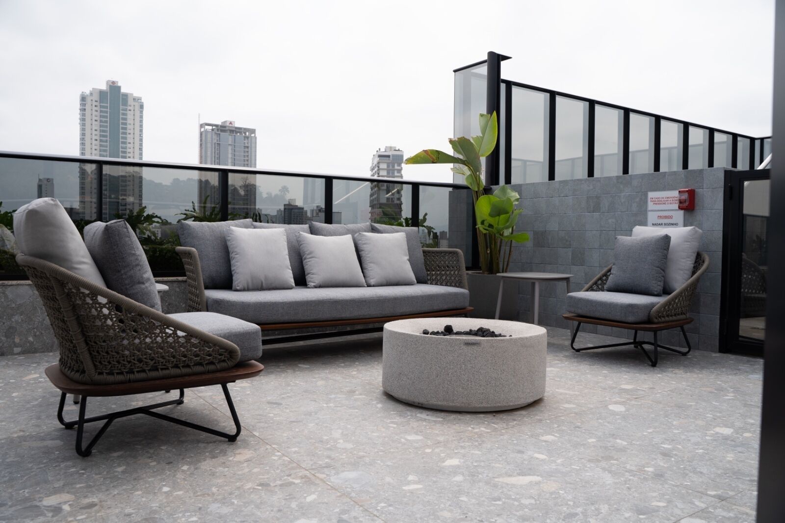 Una terraza en la azotea con un sofá gris, sillones de mimbre y una mesa redonda de piedra.