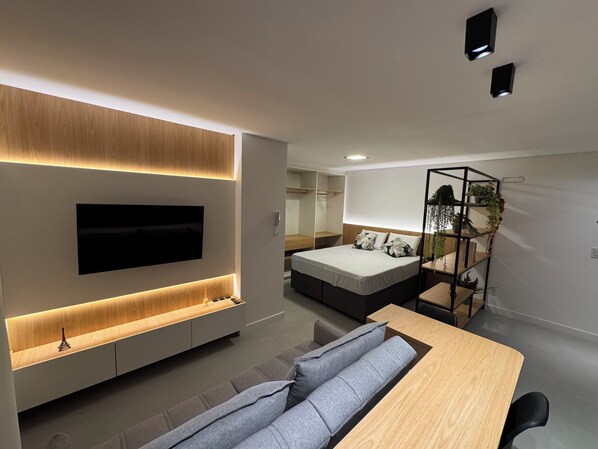 Quarto moderno com cama, mesa de cabeceira e televisão fixada na parede.