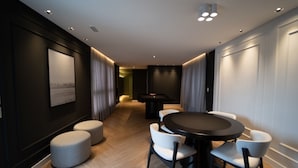 Een moderne hotelkamer met een ronde eettafel, witte stoelen en een klein voetenbankje.