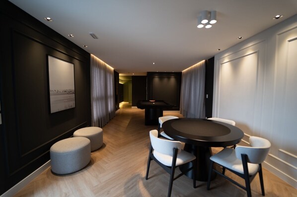 A modern hotel room with a round dining table, white chairs, and a small ottoman. - Brand new loft next to Vila Germanica (Blumenau)