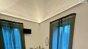 A hotel room with a bed, two chairs, a small table, and a TV on the wall. - Palermo Central Rooms (Palermo)