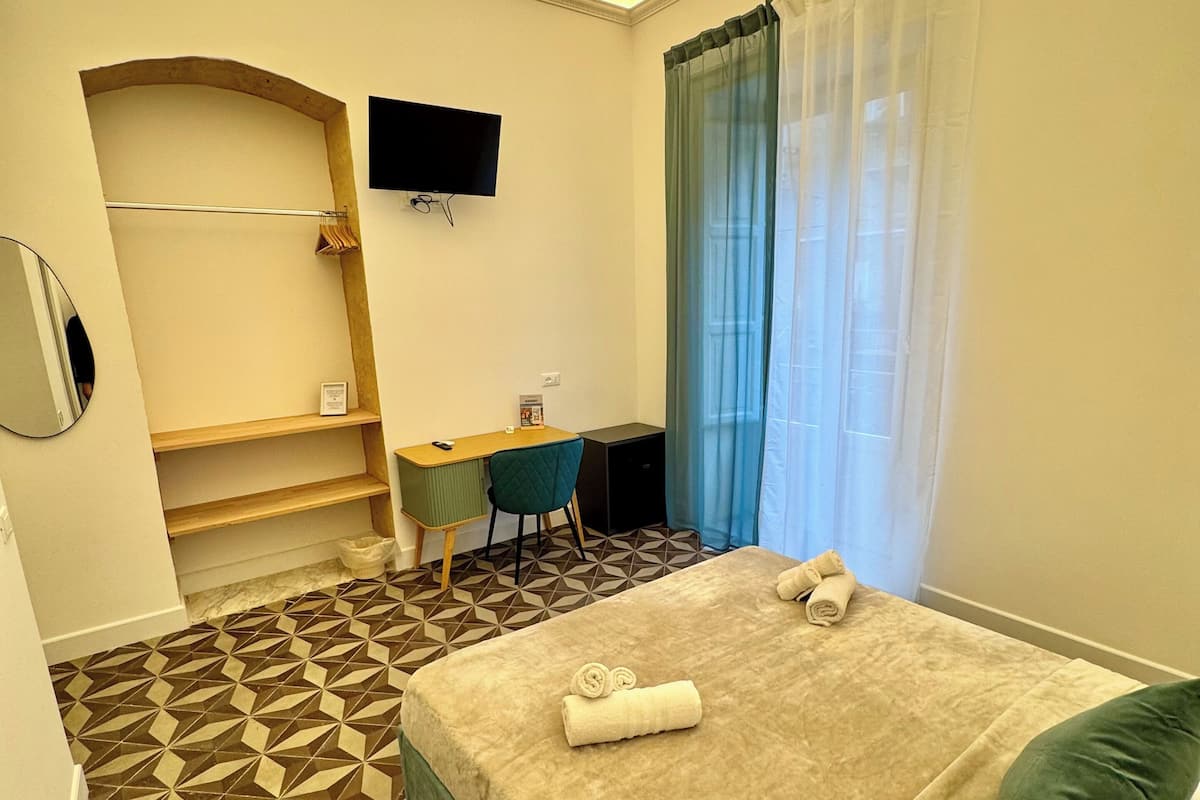 A hotel room with a bed, a desk, a chair, a TV, and a bathroom with a towel rack.