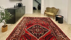 A spacious room with a large red patterned rug, a sofa, a dining area with a black cabinet, and a staircase leading to another level. - Palermo Central Rooms (Palermo)