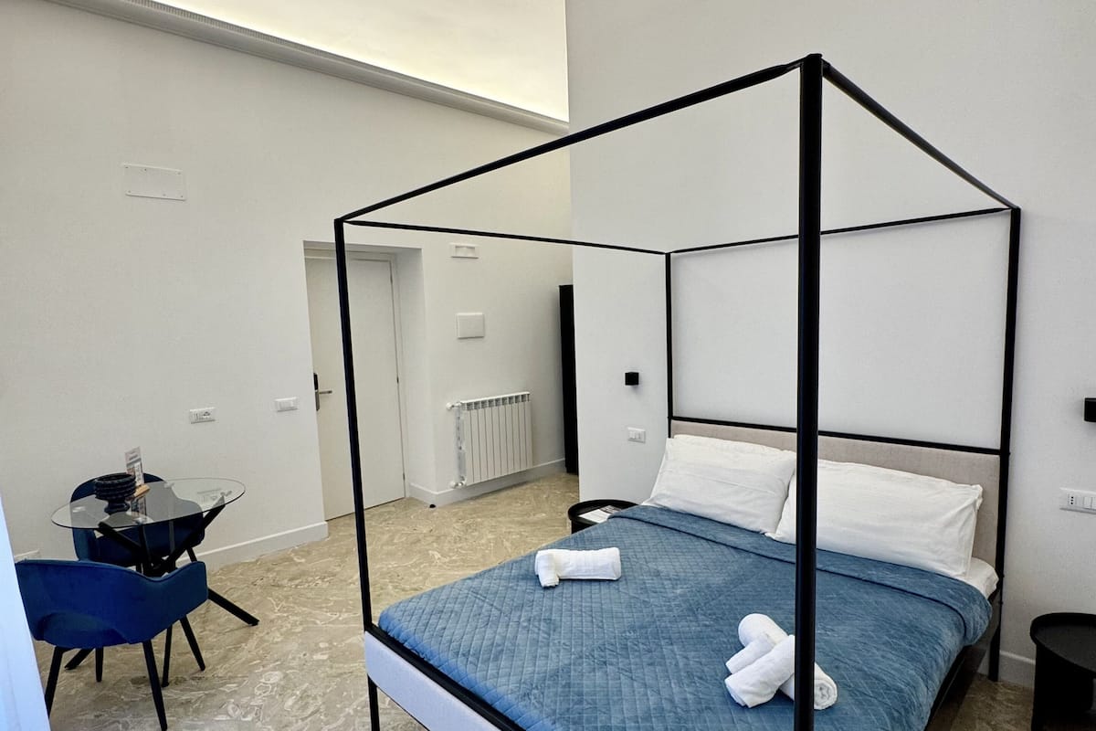 A modern bedroom with a four-poster bed, a small table with chairs, and a radiator.
