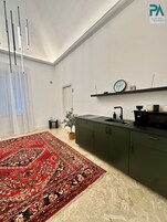 Une cuisine moderne avec des meubles de couleur verte, un four à micro-ondes et un évier. Un tapis à motifs rouges recouvre le sol, et une plante en pot est posée sur le plan de travail.