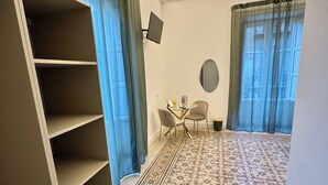 A hotel room with a large wardrobe, a small table with chairs, a flat-screen TV mounted on the wall, and a patterned carpet. - Palermo Central Rooms (Palermo)