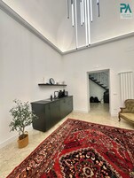 Un salon moderne avec un meuble de couleur gris foncé, un tapis à motifs rouges, une plante en pot et un escalier menant à une autre pièce.