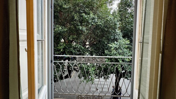A view from a balcony with a metal railing, a building with a yellow facade, and trees in the background. - Palermo Central Rooms (Palermo)