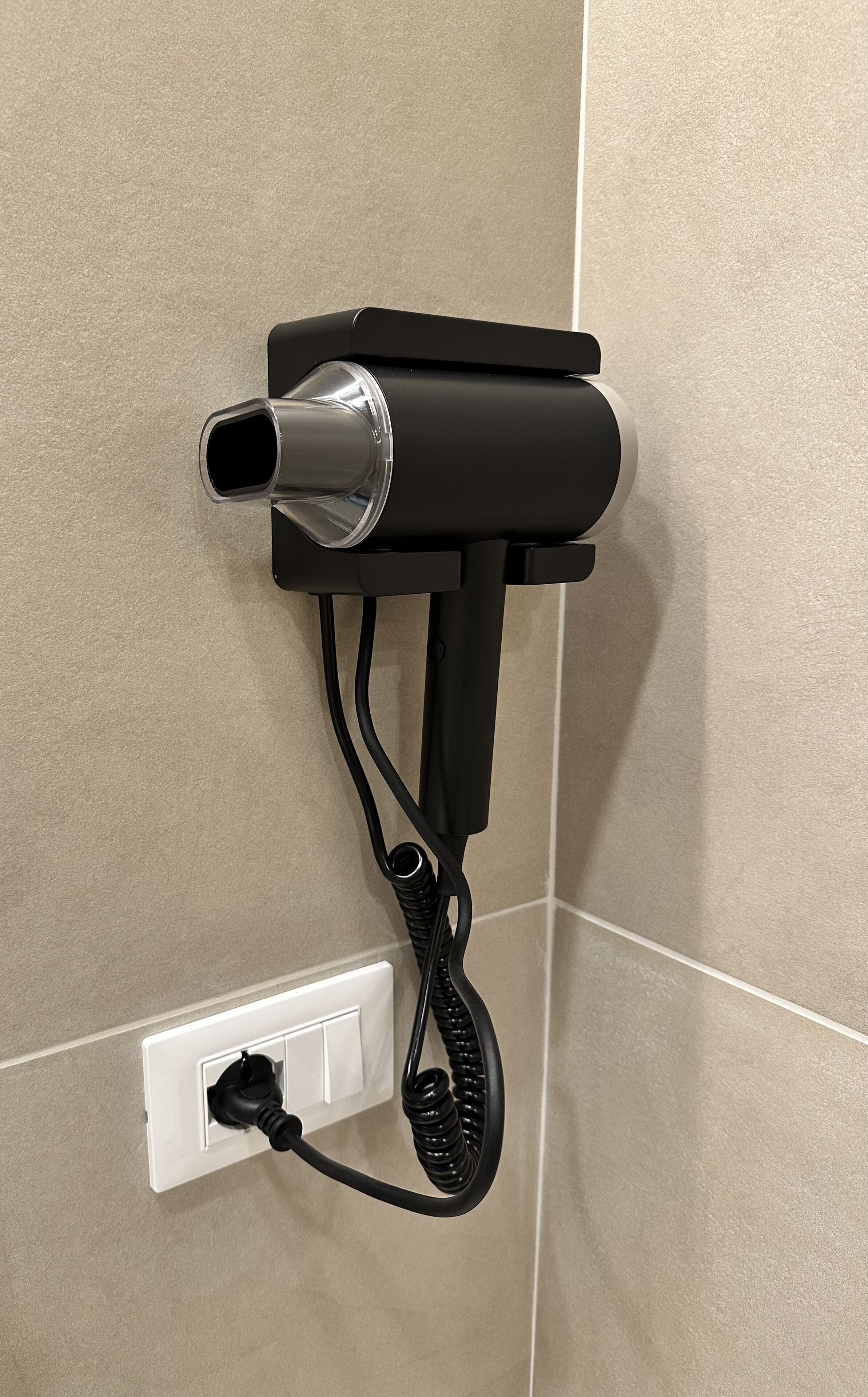 A hairdryer mounted on a wall with a power cord plugged into a wall socket.