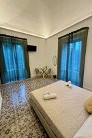 Una camera d'albergo con un letto, due sedie, un tavolino e una TV appesa al muro.