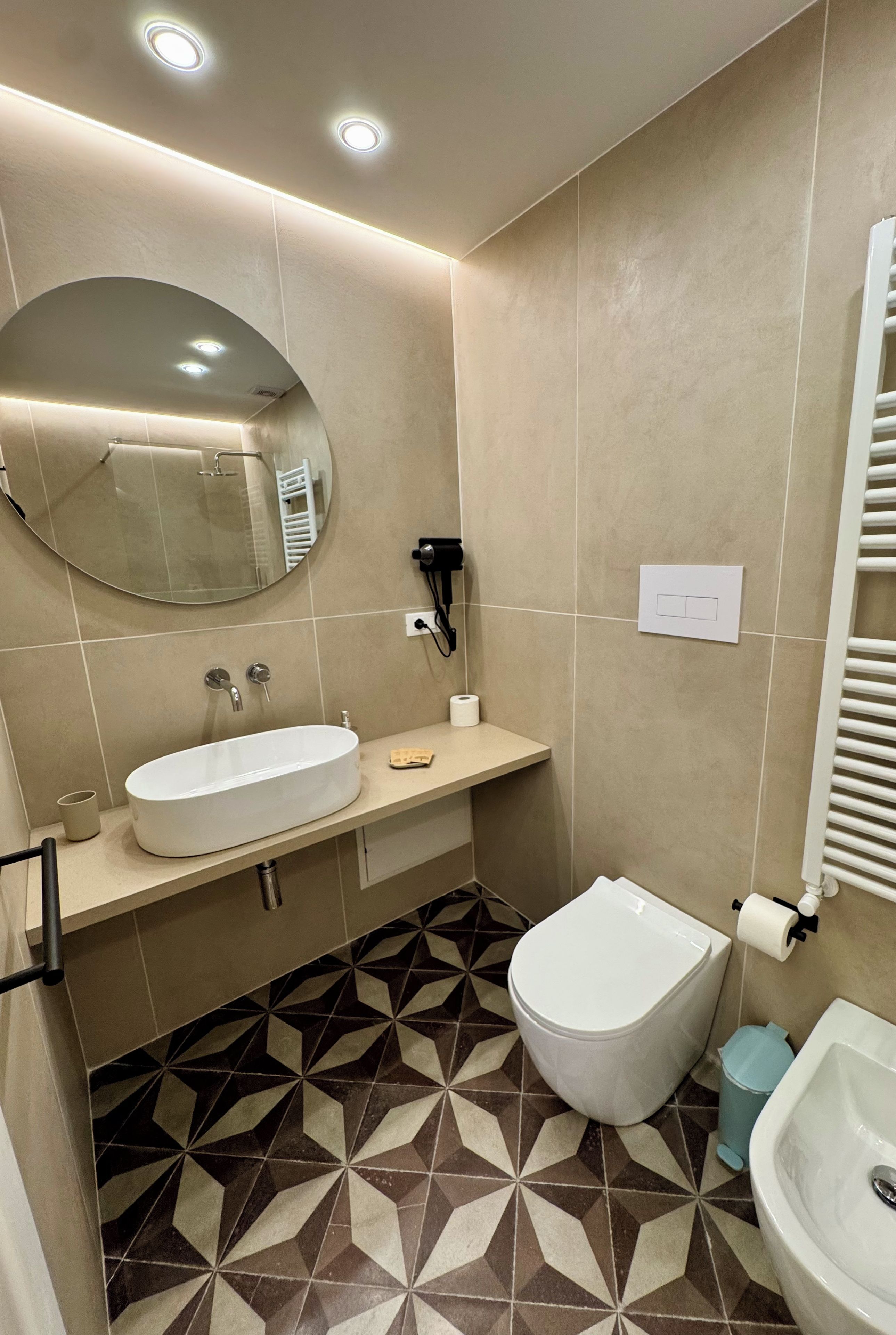 A modern bathroom with a round mirror, a sink, a bidet, and a toilet.