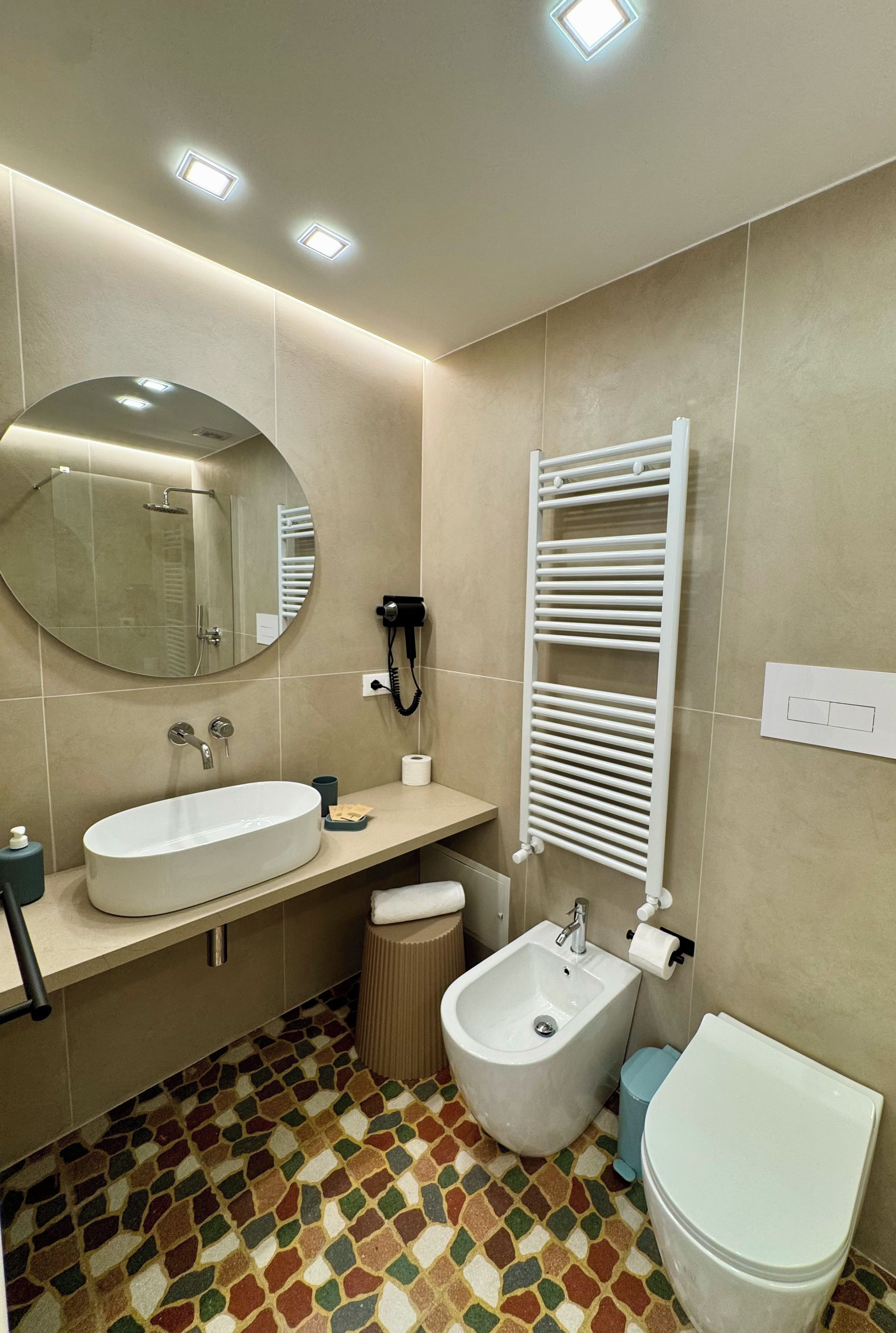 Un bagno moderno con uno specchio rotondo, un lavabo, un bidet, un water e un asciugamano riscaldato.
