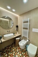 Un bagno moderno con uno specchio rotondo, un lavabo, un bidet, un water e un asciugamano riscaldato.