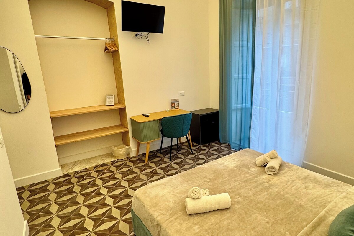 Habitación de hotel con cama, escritorio, silla, televisor y baño con perchero.