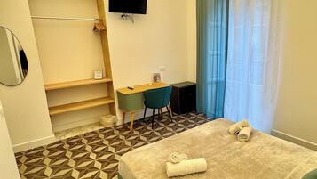 Ein Hotelzimmer mit Bett, Schreibtisch, Stuhl, Fernseher und einem Badezimmer inklusive Handtuchhalter.