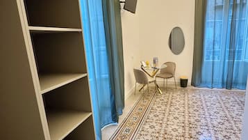 A hotel room with a large wardrobe, a small table with chairs, a flat-screen TV mounted on the wall, and a patterned carpet.