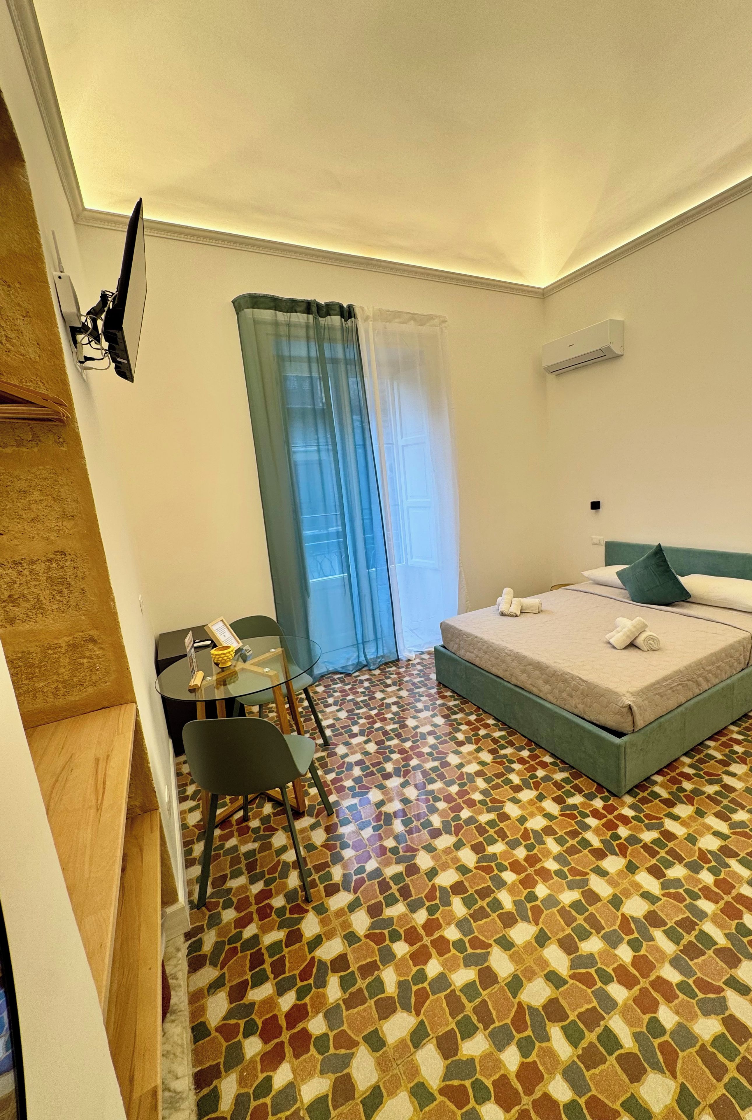 Habitación de hotel con cama, escritorio, silla, mesita y ventana con cortinas.