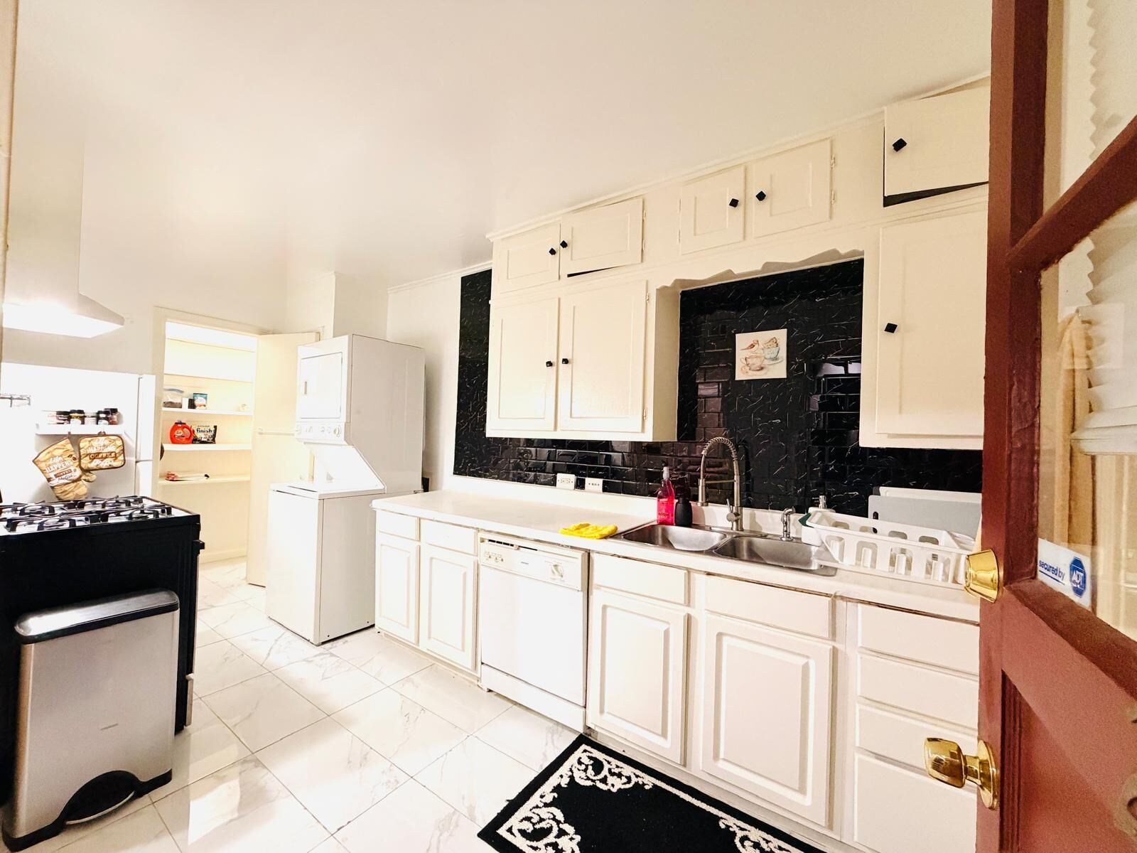 A kitchen with white cabinets, a black backsplash, a gas stove, and a refrigerator.