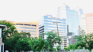 Une vue urbaine avec des bâtiments modernes, dont un imposant bâtiment en verre portant l’inscription « BAYLOR CLINIC ».