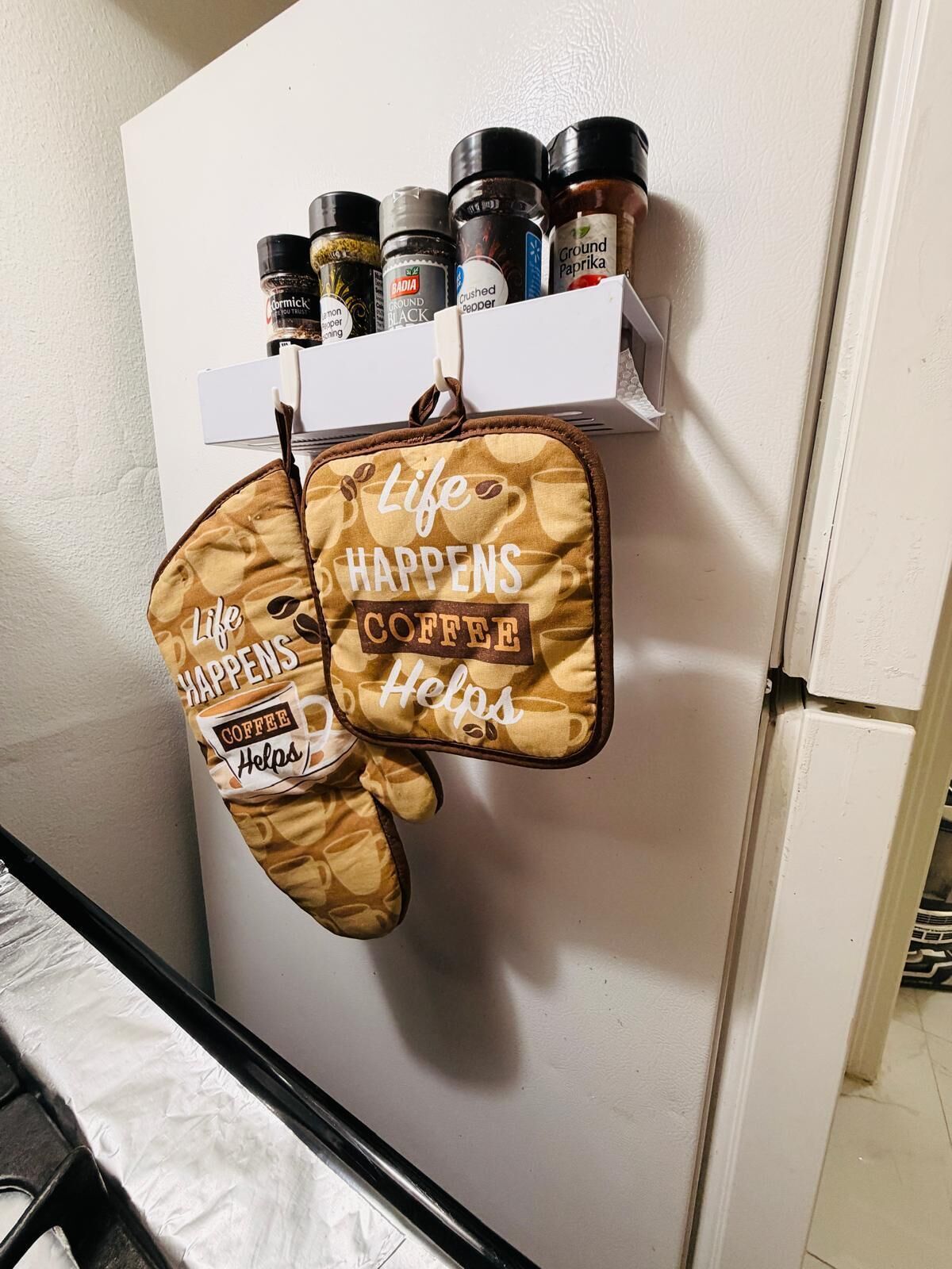 Una cucina con un ripiano portaspezie pieno di spezie diverse e due presine appese a un gancio a tema caffè.