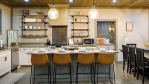 A kitchen with a central island, bar stools, a microwave, and hanging pendant lights.