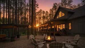A lodge with a fire pit, outdoor seating, and a deck overlooking a forest.