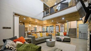 A spacious living area with a high ceiling, a fireplace, and a kitchen in the background.
