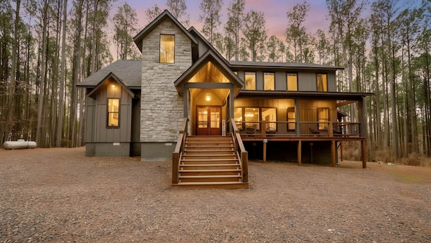 A two-story log cabin with a stone exterior, a wooden deck, and a staircase leading to the entrance.