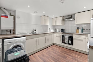 A modern kitchen with white cabinets, a built-in oven, a dishwasher, and a coffee maker. - Central House, Near Train & Fun! (Worcestershire)
