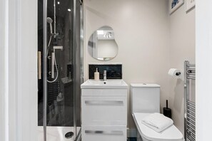 A modern bathroom with a glass-enclosed shower, a white sink with a marble countertop, a toilet, and a towel rack.