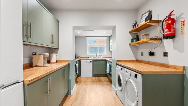 Een kleine keuken met een wasmachine, houten werkbladen en een klein raam.