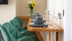 Een eettafel gedekt met borden, kommen en glazen, een vaas met bloemen en een groene fauteuil.