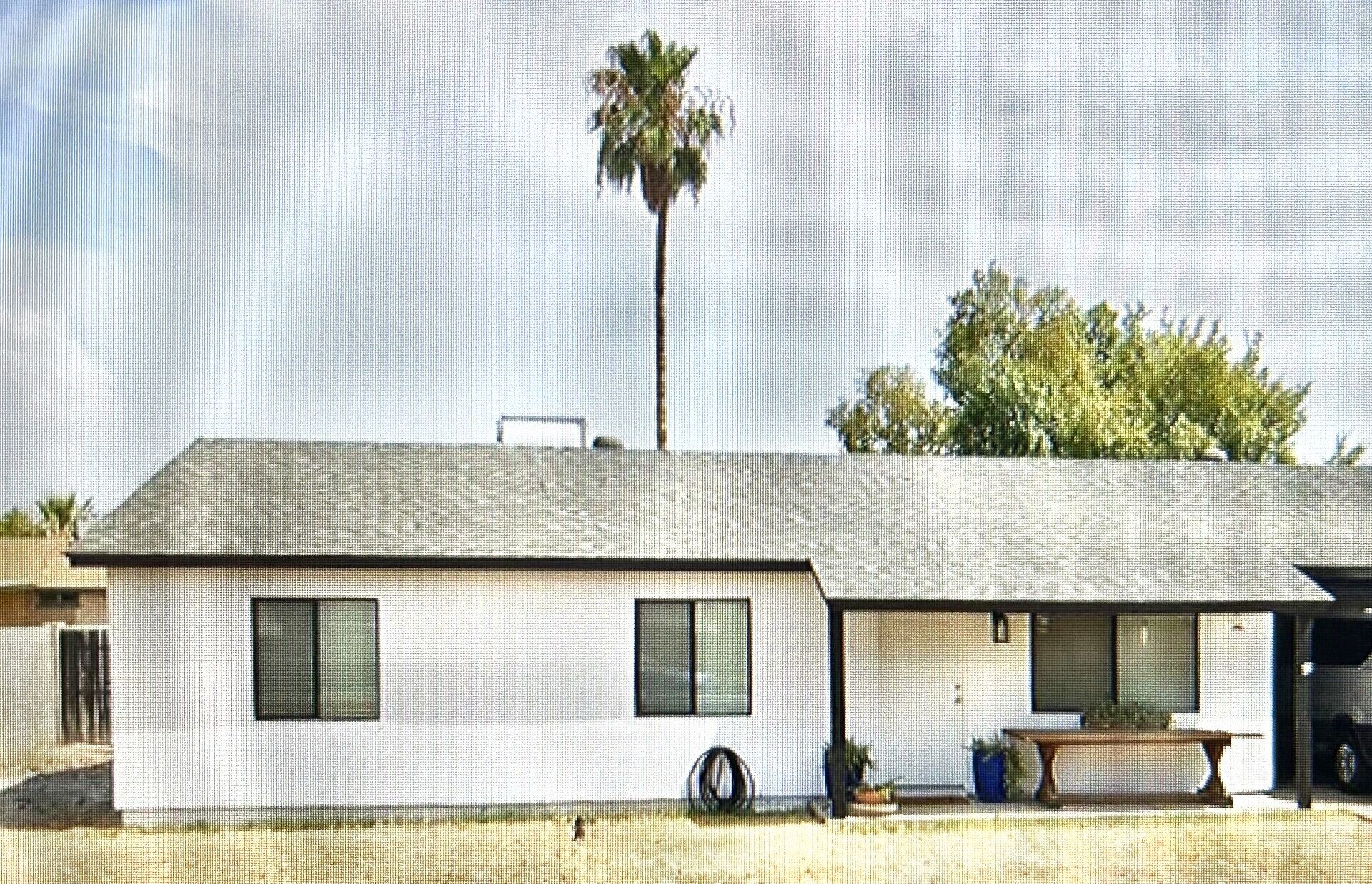 A single-story building with a flat roof, two windows, and a small porch area with a table and chairs.