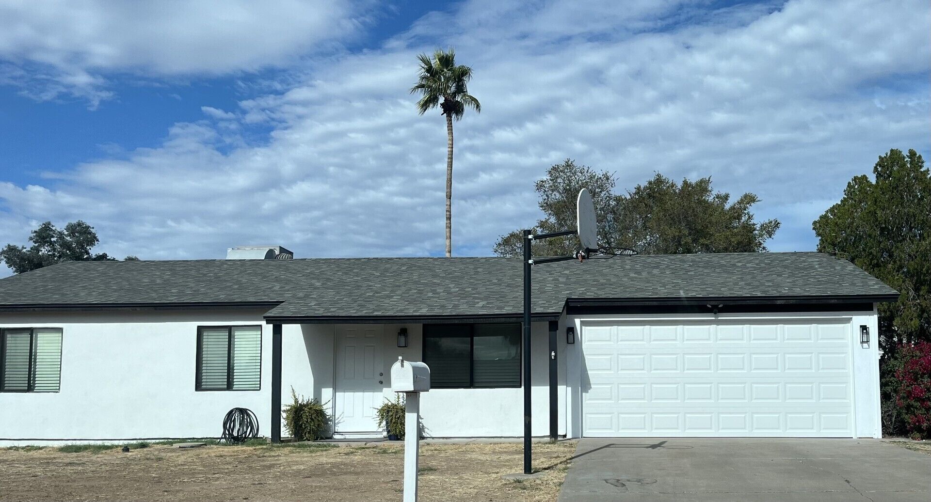 A single-story house with a garage, a satellite dish, and a palm tree in the background.
