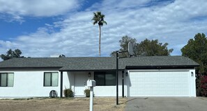 Une maison de plain-pied avec un garage, une antenne parabolique et un palmier en arrière-plan.