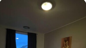 A small, dimly lit room with two single beds, a nightstand, a chair, and a painting on the wall. - 4-bedroom house in Höfn í Hornafirði (Höfn í Hornafirði)