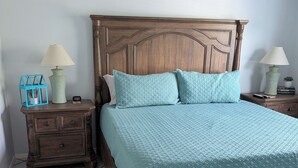 Un dormitorio con cama de madera, dos mesitas de noche, ventilador de techo y suelo de baldosas.