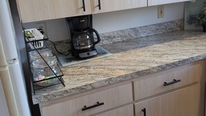 Una cocina con armarios de madera clara, encimera de granito y cafetera.