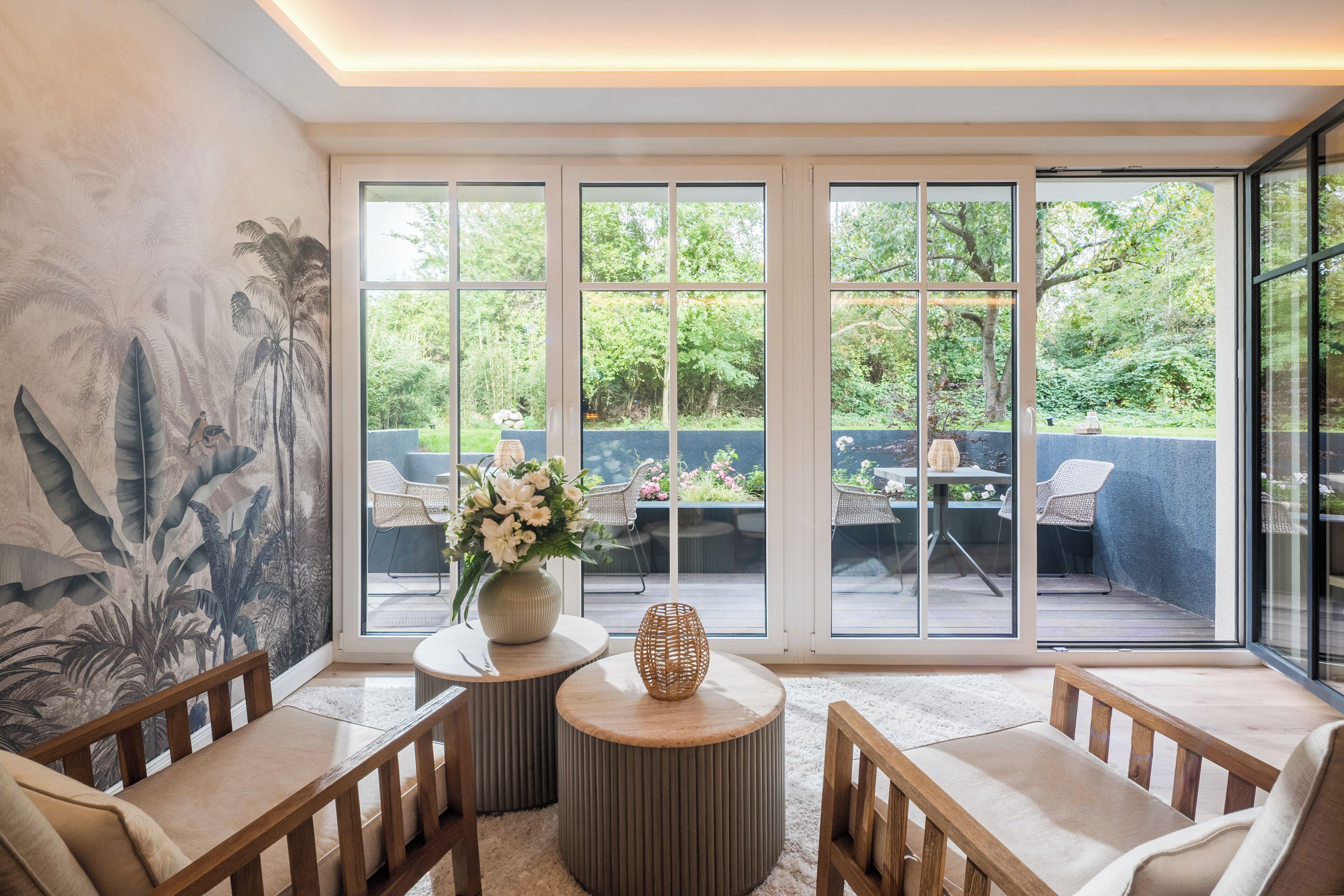 A modern living room with a large window, a decorative wall mural, and a seating area with a round table and chairs.