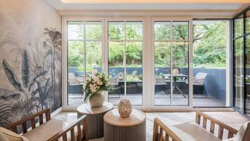 A modern living room with a large window, a decorative wall mural, and a seating area with a round table and chairs.