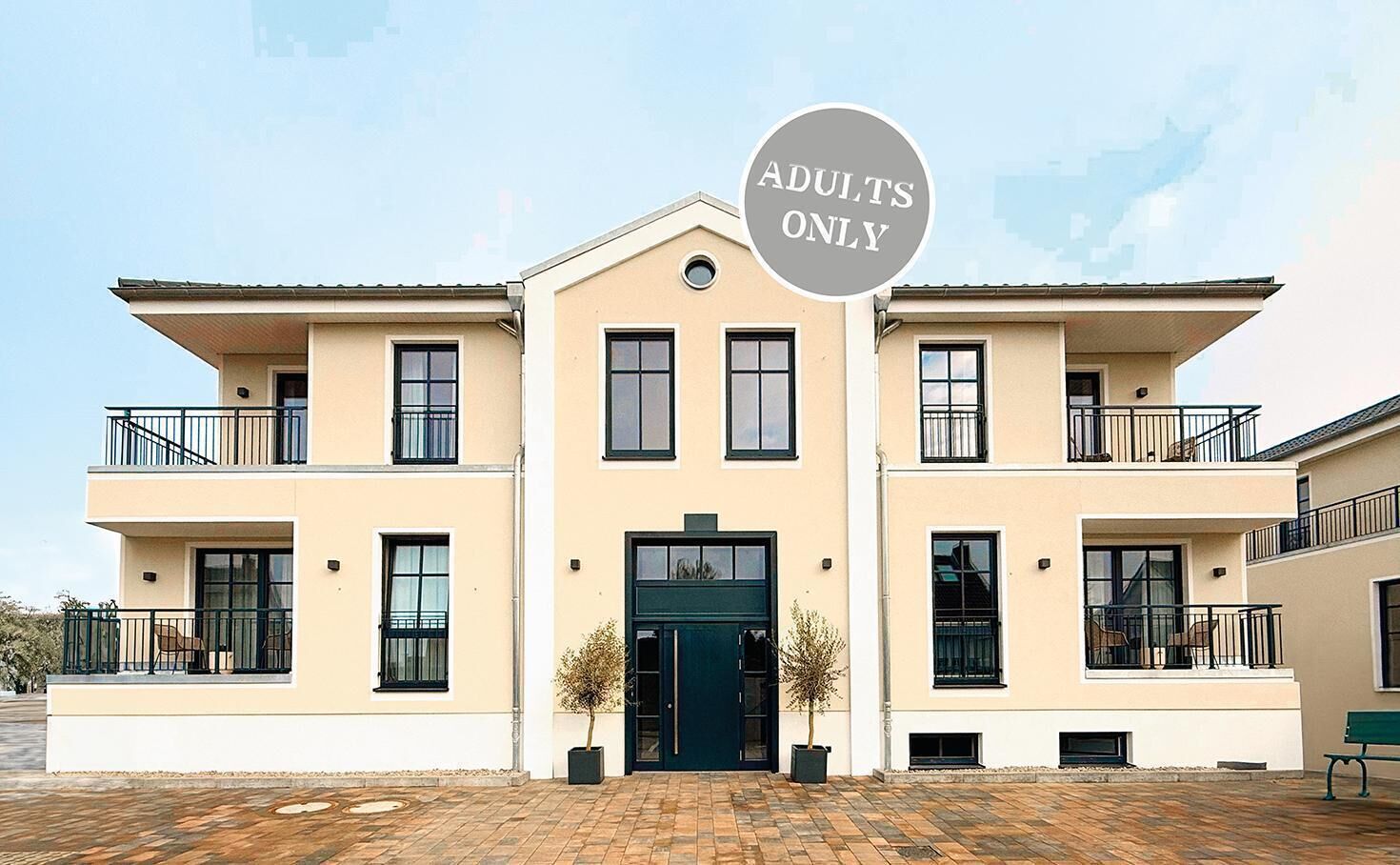 A two-story building with a central entrance, balconies on each floor, and a sign indicating 'ADULTS ONLY'.