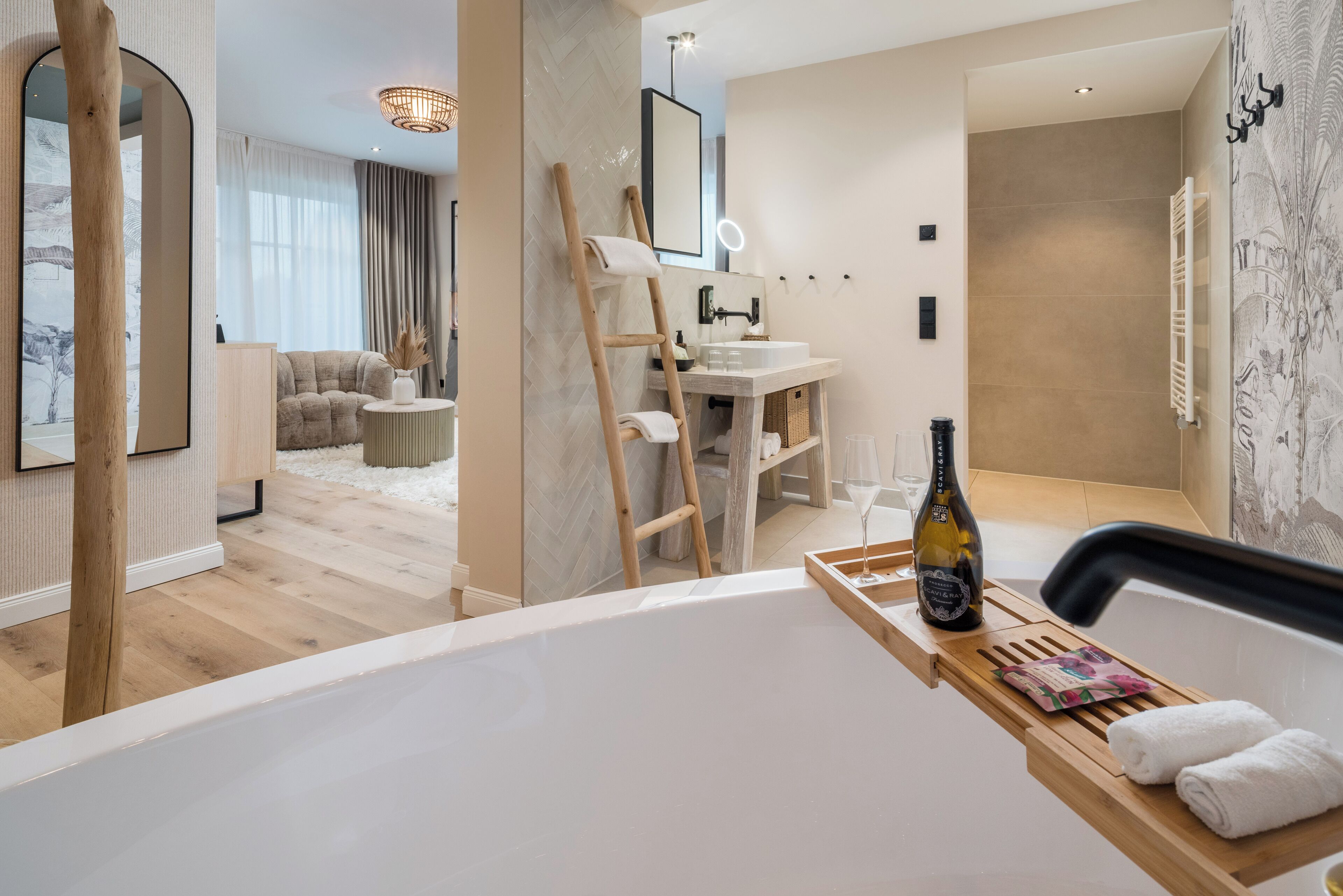 Een moderne badkamer met een badkuip, een houten trapje, een handdoekhouder en een fles champagne op een dienblad.