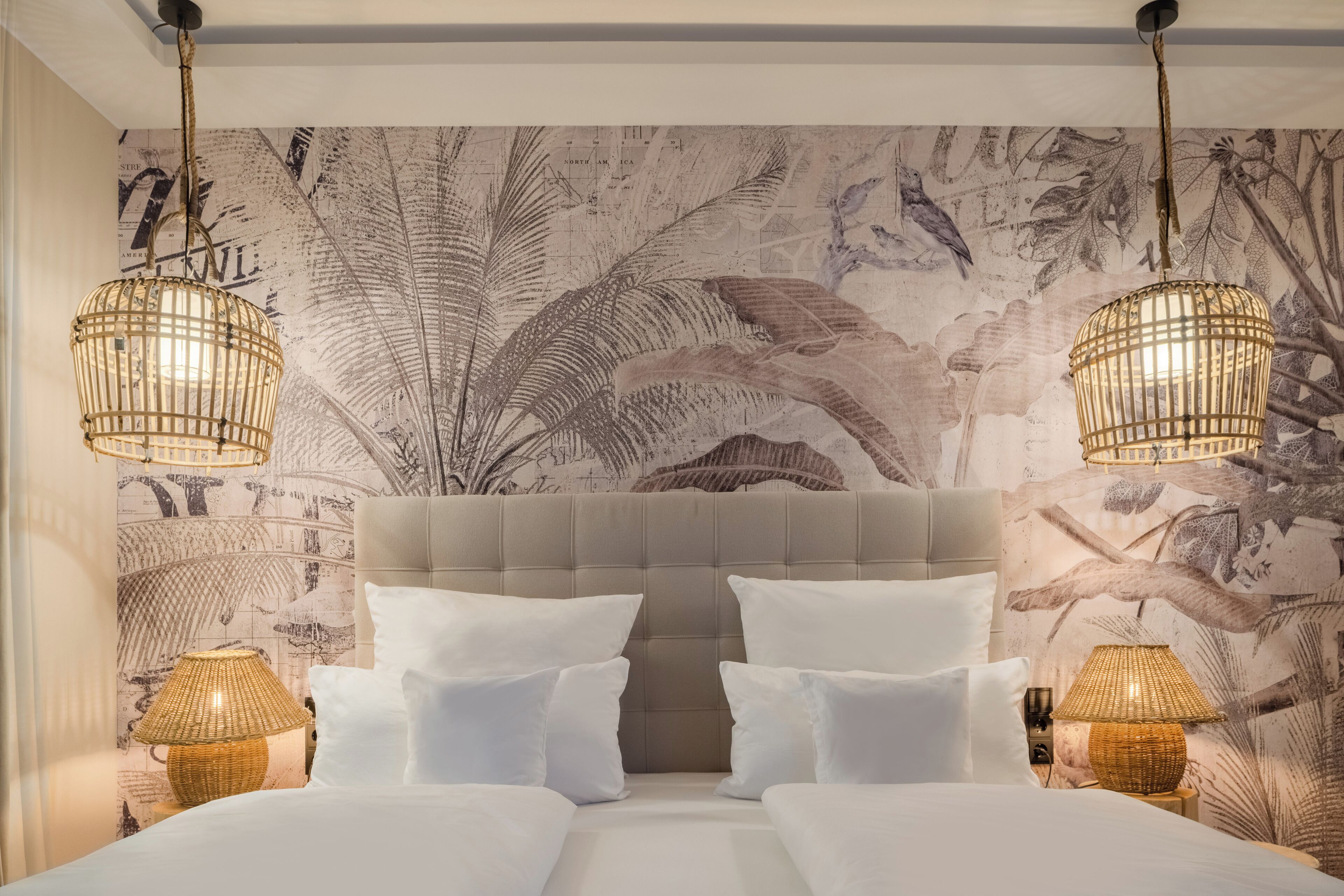 A hotel room with a large bed, two bedside tables with lamps, a tufted headboard, and a wall mural with tropical foliage.