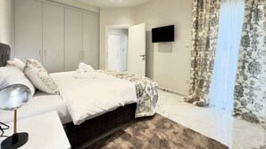 A bedroom with a bed, a TV, a wardrobe, and a door leading to another room.