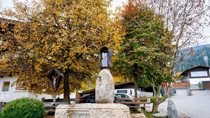 Monumento de piedra con inscripciones, rodeado de árboles y bancos en un parque.