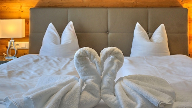 Una cama bien hecha con dos toallas dispuestas en forma de corazón.